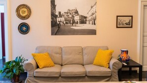 A living room with a sofa, cushions, a framed photograph, and a vase on a table. - GuestHost - Casa Arezzo al Duomo (Modica)