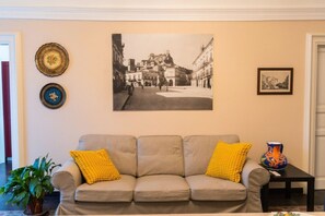 A living room with a sofa, cushions, a framed photograph, and a vase on a table. - GuestHost - Casa Arezzo al Duomo (Modica)
