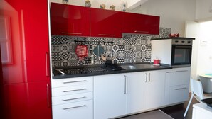 A kitchen with red cabinets, a black countertop, and patterned backsplash tiles. - GuestHost - Casa Arezzo al Duomo (Modica)