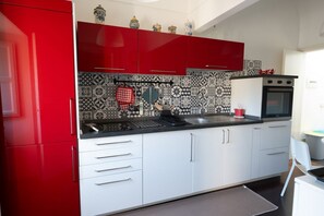 A kitchen with red cabinets, a black countertop, and patterned backsplash tiles. - GuestHost - Casa Arezzo al Duomo (Modica)