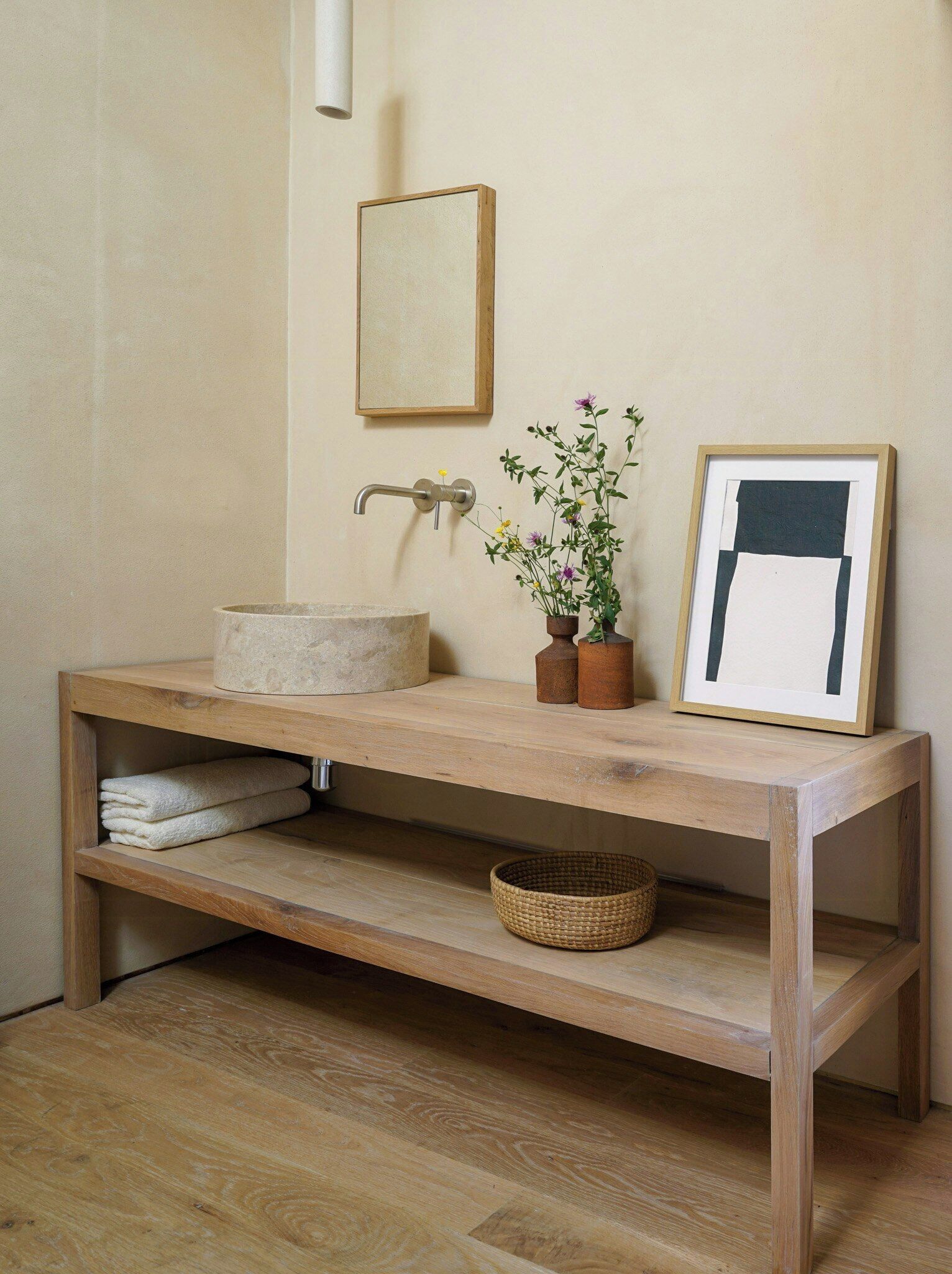 Une coiffeuse en bois avec un lavabo, un tableau encadré et une plante en pot.