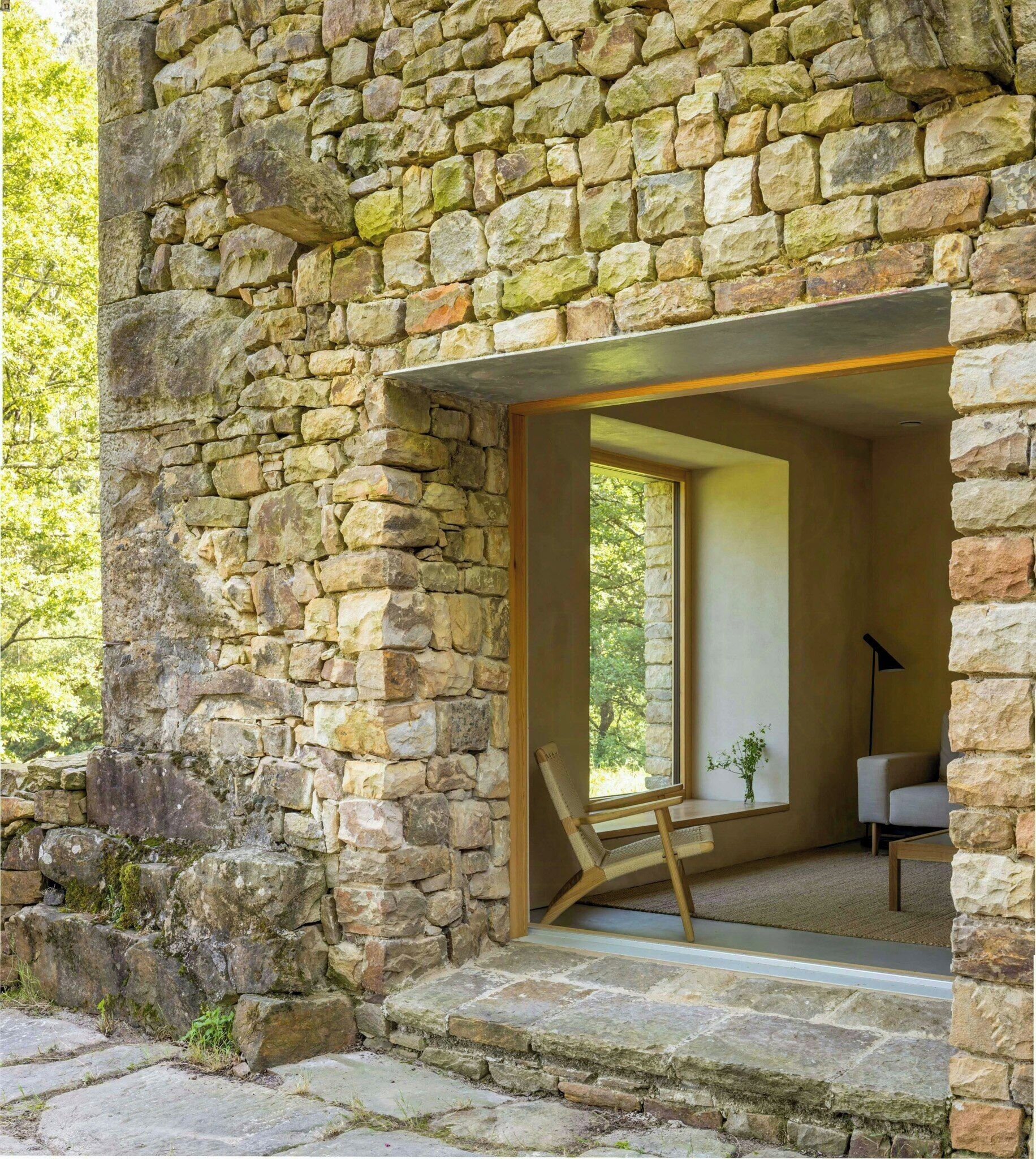 A stone building with a large window and a wooden chair inside.