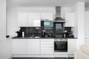 A modern kitchen with white cabinets, a black countertop, a stainless steel range hood, and a built-in oven. - Bright 2BD 2bath Sleeps 6 London View (London)