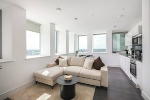 A modern living room with a sectional sofa, a round coffee table, and a view of the city through large windows.
