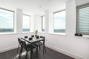 A modern dining area with a table set for four, large windows with blinds, and a city view.