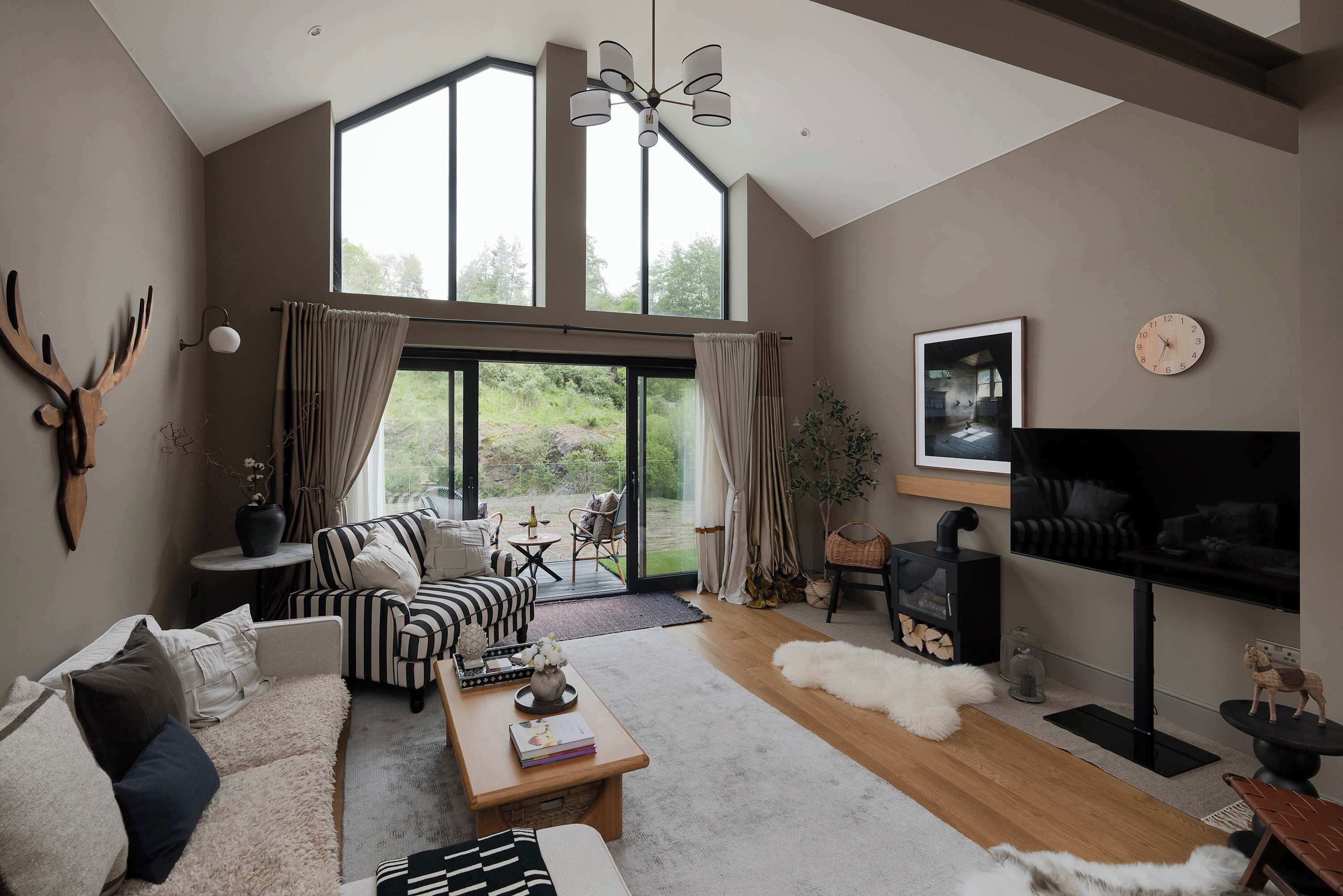 Una sala de estar moderna con un ventanal grande, una chimenea, un televisor y un rincón de estar acogedor.