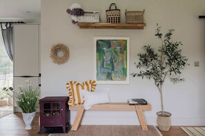 Et værelse med en træbænk, en potteplante, en vægmonteret hylde med fletter, et indrammet abstrakt billede og en dekorativ krans.
