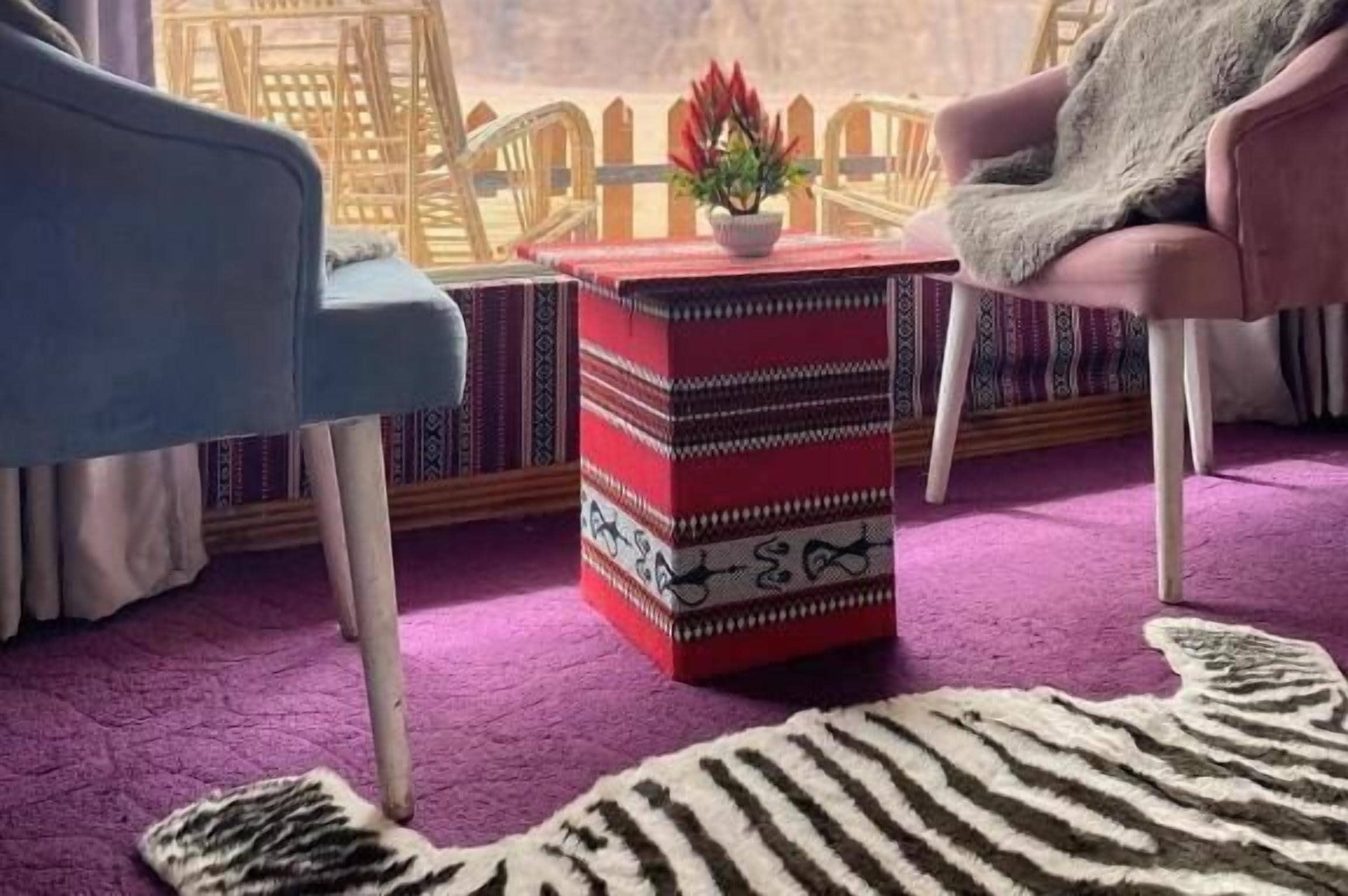 Una habitación con alfombra morada, un reposapiés a rayas, una silla azul y una silla rosa.