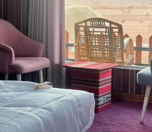 Habitación de hotel con una cama, una silla, una mesita y vistas a un paisaje desértico.