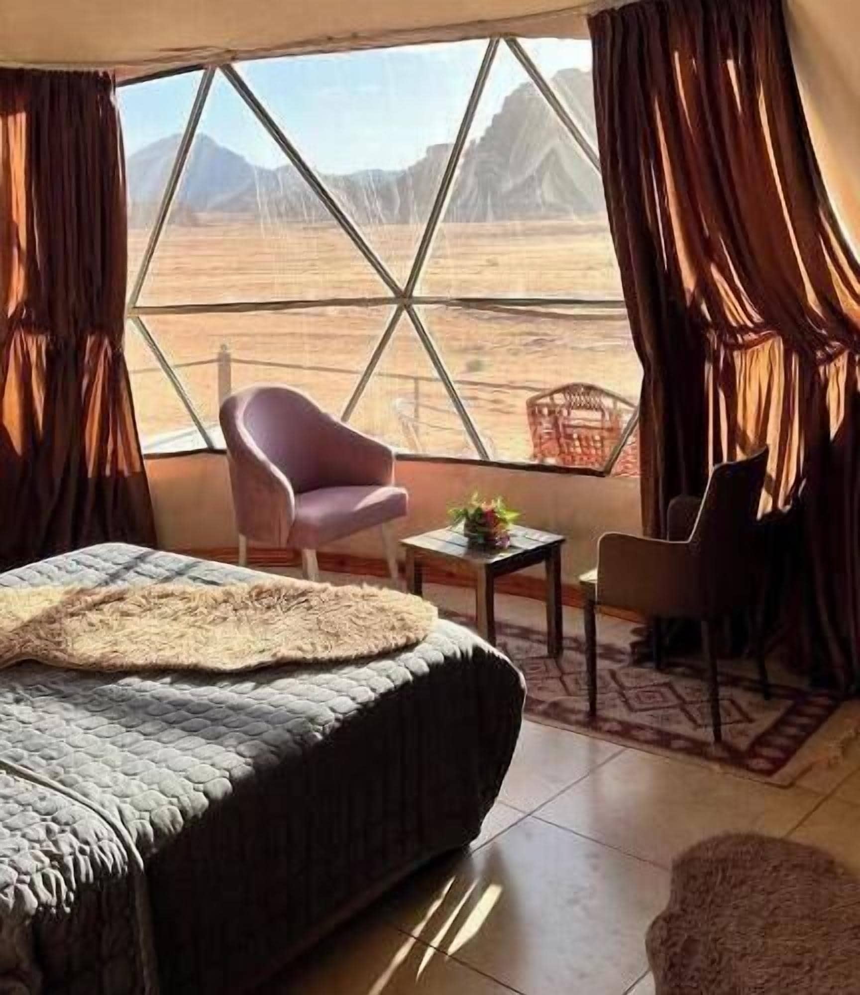 Une chambre avec un lit, une chaise, une petite table et une vue sur un paysage désertique, visible à travers de grandes fenêtres.
