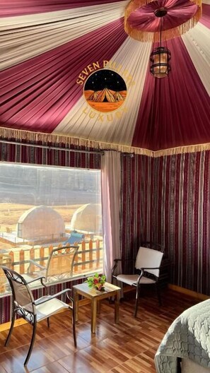 A room with a view of a desert landscape, a balcony with a wooden fence, and a table with chairs.