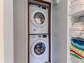 Une petite buanderie équipée de deux machines à laver superposées et d’un étendoir à linge.