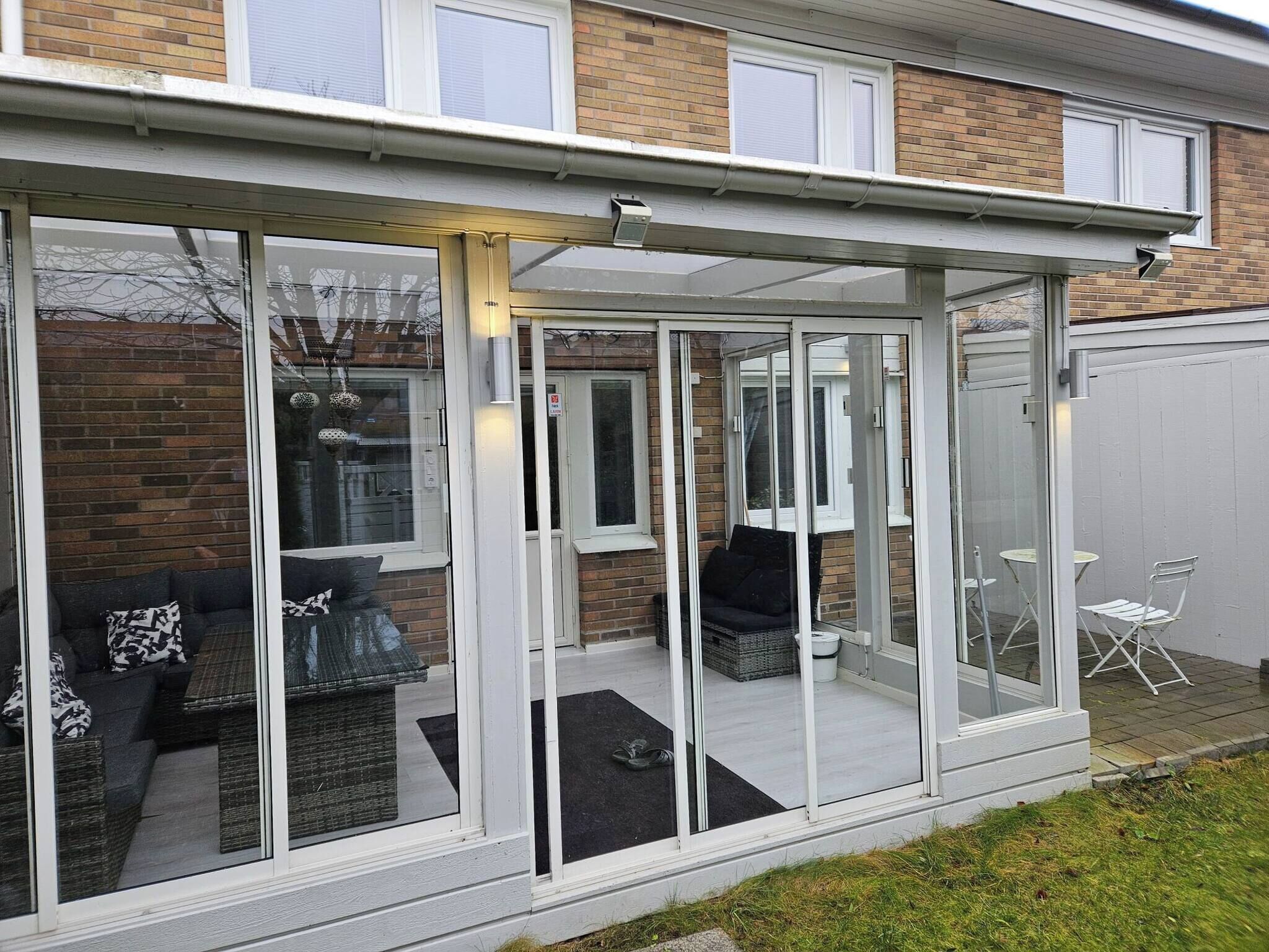 A glass-enclosed patio with outdoor furniture and a white door.