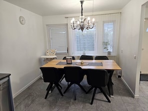 Un comedor con una mesa de madera, sillas negras, una araña y un reloj en la pared.