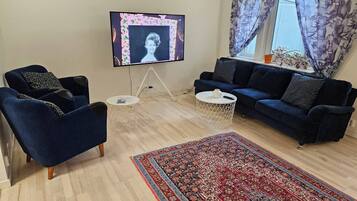 Una sala de estar con televisor, dos sofás, una mesa de centro y un tapete estampado.