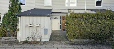A residential building with a front door, a small shed, and a hedge.