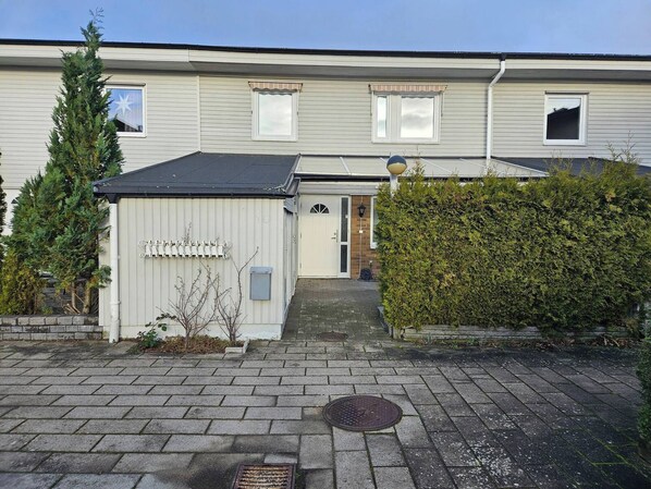 A residential building with a front door, a small shed, and a hedge.