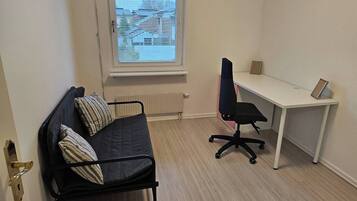A small, furnished room with a bed, a desk, and a chair.
