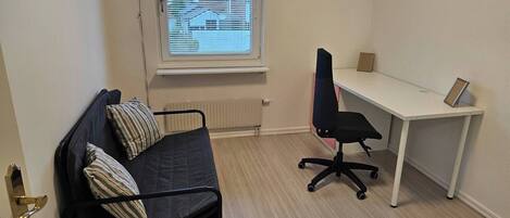 A small, furnished room with a bed, a desk, and a chair.