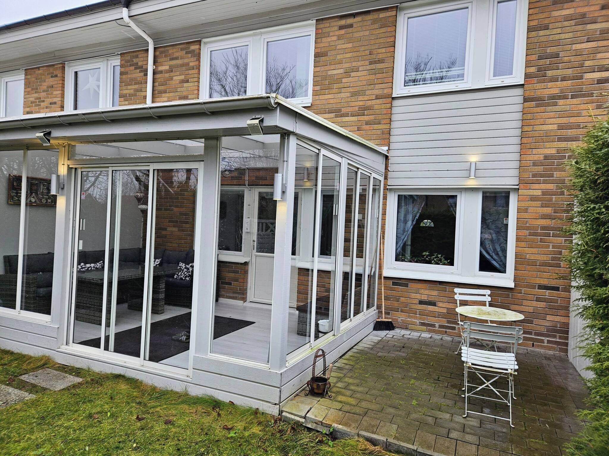 A modern house with a glass conservatory, a brick exterior, and a small patio with a table and chairs.