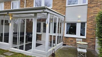 A modern house with a glass conservatory, a brick exterior, and a small patio with a table and chairs.