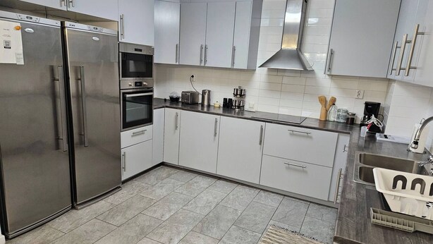 Een moderne keuken met roestvrijstalen apparatuur, witte kastjes en een betegelde spatwand.