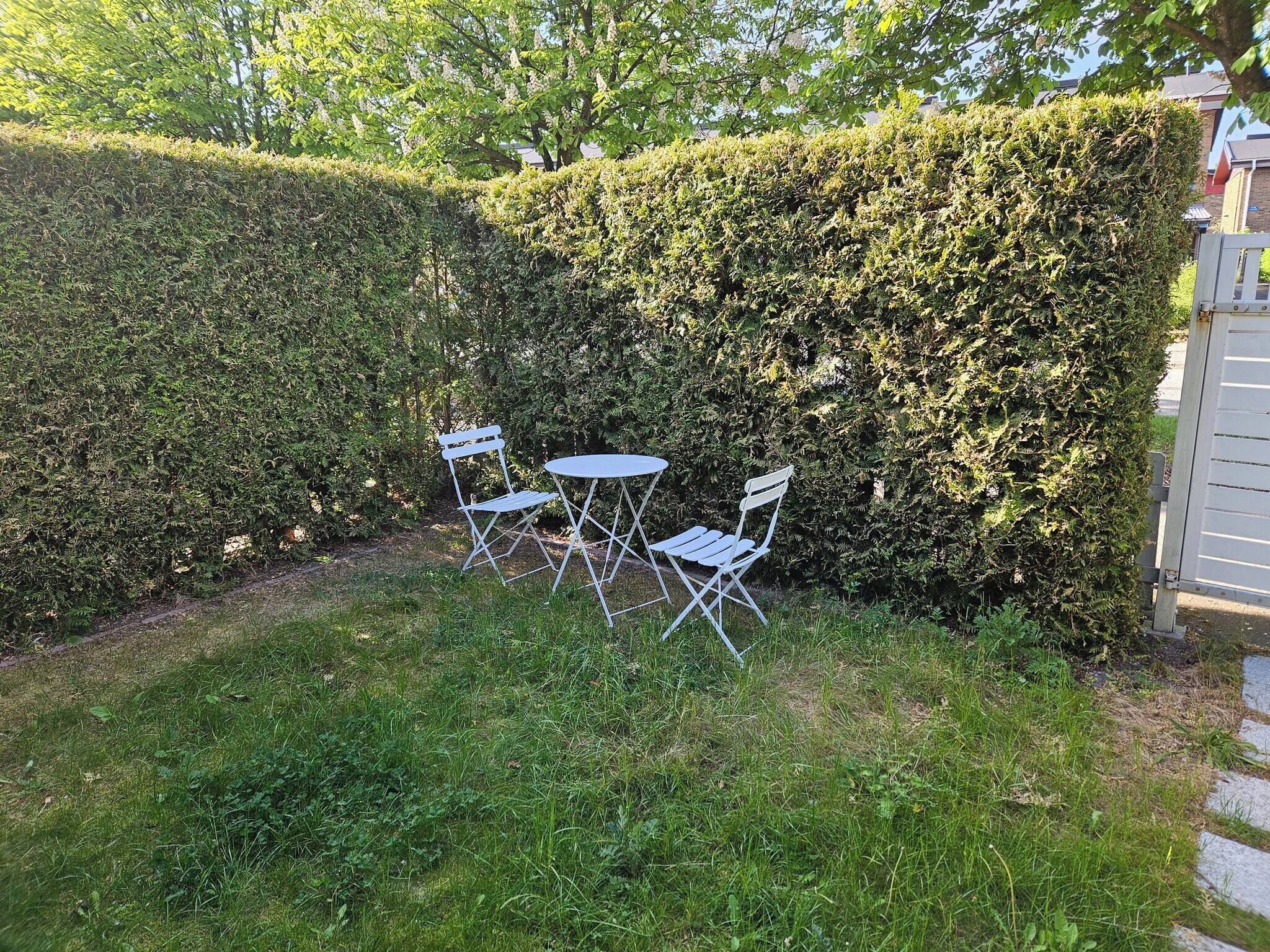 Un jardín con seto, una mesita y dos sillas.