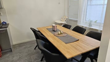 A dining area with a wooden table, black chairs, a chandelier, a clock, and a window with blinds.