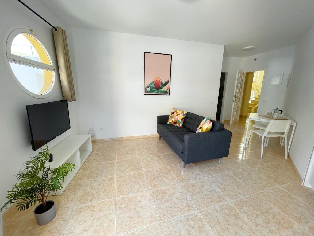 Una sala de estar con un sofá, un televisor, una planta en maceta y un ventanal con cortinas.