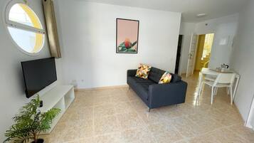 Una sala de estar con un sofá, un televisor, una planta en maceta y un ventanal con cortinas.