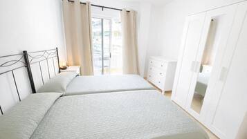 A bedroom with two beds, a wardrobe, and a balcony.