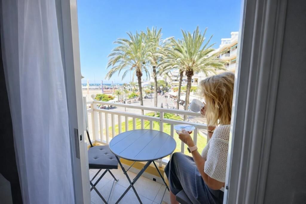 A balcony with a view of palm trees and buildings, a small round table, and a chair.