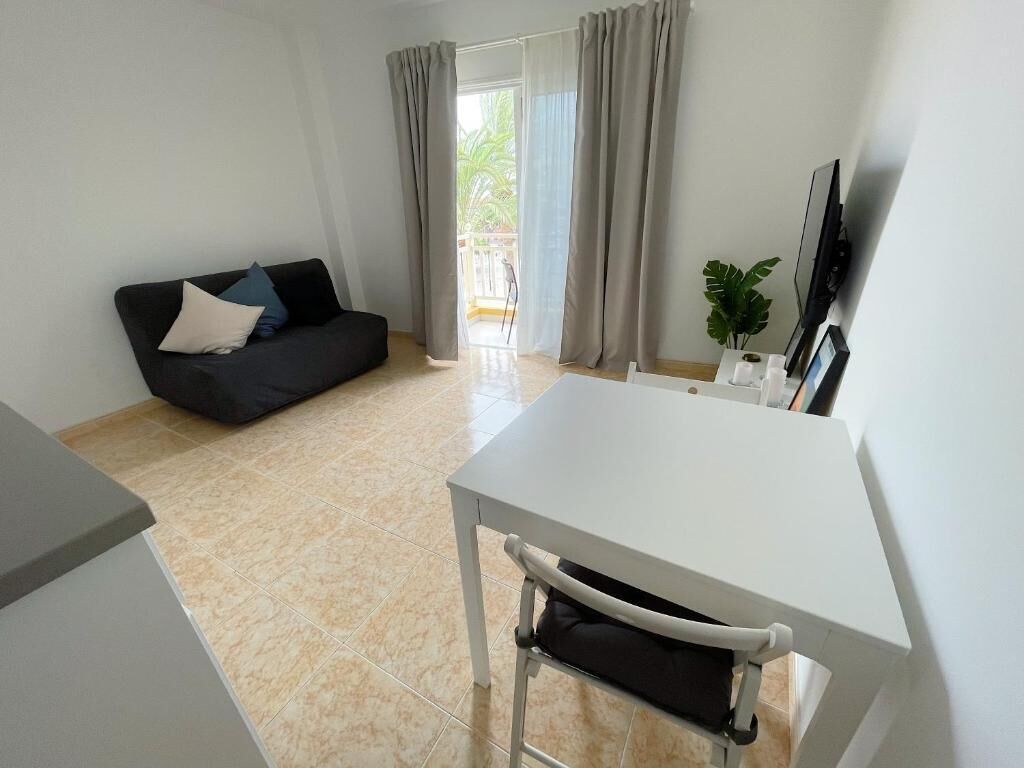 Una sala de estar moderna con una mesa blanca, un sofá negro y un ventanal con cortinas.