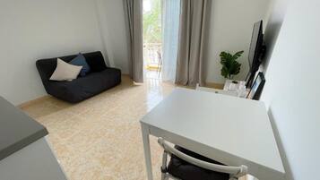 Una sala de estar moderna con una mesa blanca, un sofá negro y un ventanal con cortinas.