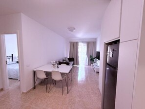 A modern kitchen with a refrigerator, a dining table with chairs, and a window with curtains. - Edificio Don Diego (Los Cristianos)