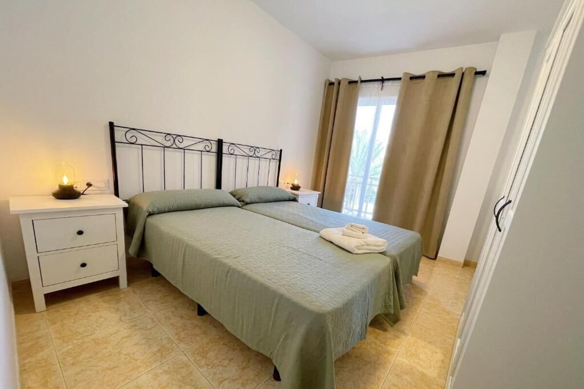 Un dormitorio con cama, mesitas de noche y una ventana con cortinas.