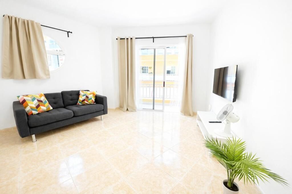 A modern living room with a sofa, a flat-screen TV, a fan, and a potted plant.
