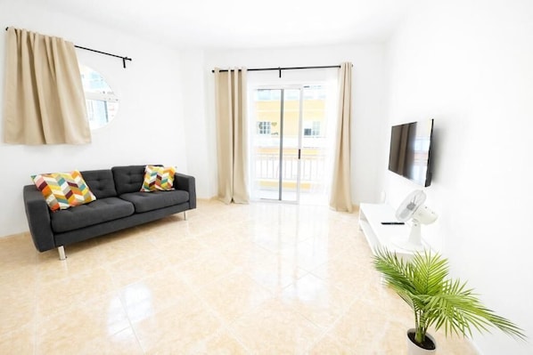 A modern living room with a sofa, a flat-screen TV, a fan, and a potted plant. - Edificio Don Diego (Los Cristianos)