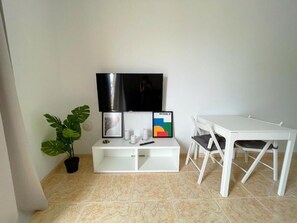 Ein Zimmer mit einem weißen TV-Schrank, einem Flachbildfernseher, einem weißen Tisch und einer Topfpflanze.