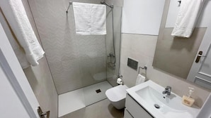 Un baño moderno con cabina de ducha de vidrio, inodoro y lavamanos con espejo.