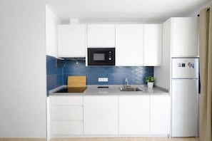 A modern kitchen with white cabinets, a black microwave, a stainless steel sink, and a built-in refrigerator. - Edificio Don Diego (Los Cristianos)