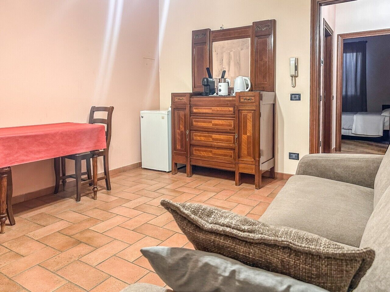 Een knus woongedeelte met een eettafel, een bank, een houten dressoir en een kleine koelkast.