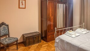 Une chambre avec une armoire en bois, une chaise, une table de chevet avec des serviettes et un luminaire suspendu.