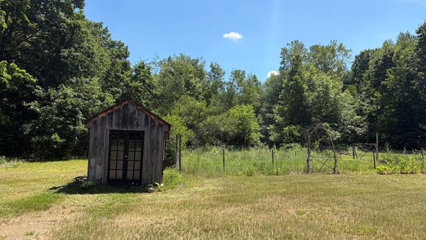 A rustic wooden shed in a grassy field with trees in the background. - 3-Bedroom Getaway Between Saratoga Springs & Lake George (Gansevoort)