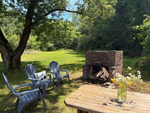 A wooden table with a vase of flowers, two Adirondack chairs, and a brick fireplace in a grassy outdoor area. - 3-Bedroom Getaway Between Saratoga Springs & Lake George (Gansevoort)