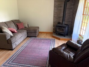 A living room with a sectional sofa, a leather armchair, a patterned rug, and a wood-burning stove. - 3-Bedroom Getaway Between Saratoga Springs & Lake George (Gansevoort)