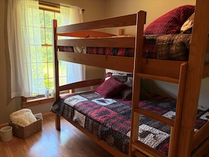 A bunk bed with a quilt, a window with curtains, and a basket on the floor.