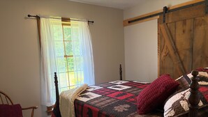 A bedroom with a bed, a window with curtains, a wooden chair, and a quilted bedspread. - 3-Bedroom Getaway Between Saratoga Springs & Lake George (Gansevoort)
