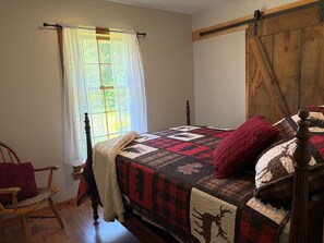 A bedroom with a bed, a window with curtains, a wooden chair, and a quilted bedspread. - 3-Bedroom Getaway Between Saratoga Springs & Lake George (Gansevoort)