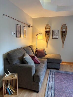 A modern living room with a grey sectional sofa, a standing floor lamp, and two wall-mounted Adirondack chairs. - 3-Bedroom Getaway Between Saratoga Springs & Lake George (Gansevoort)